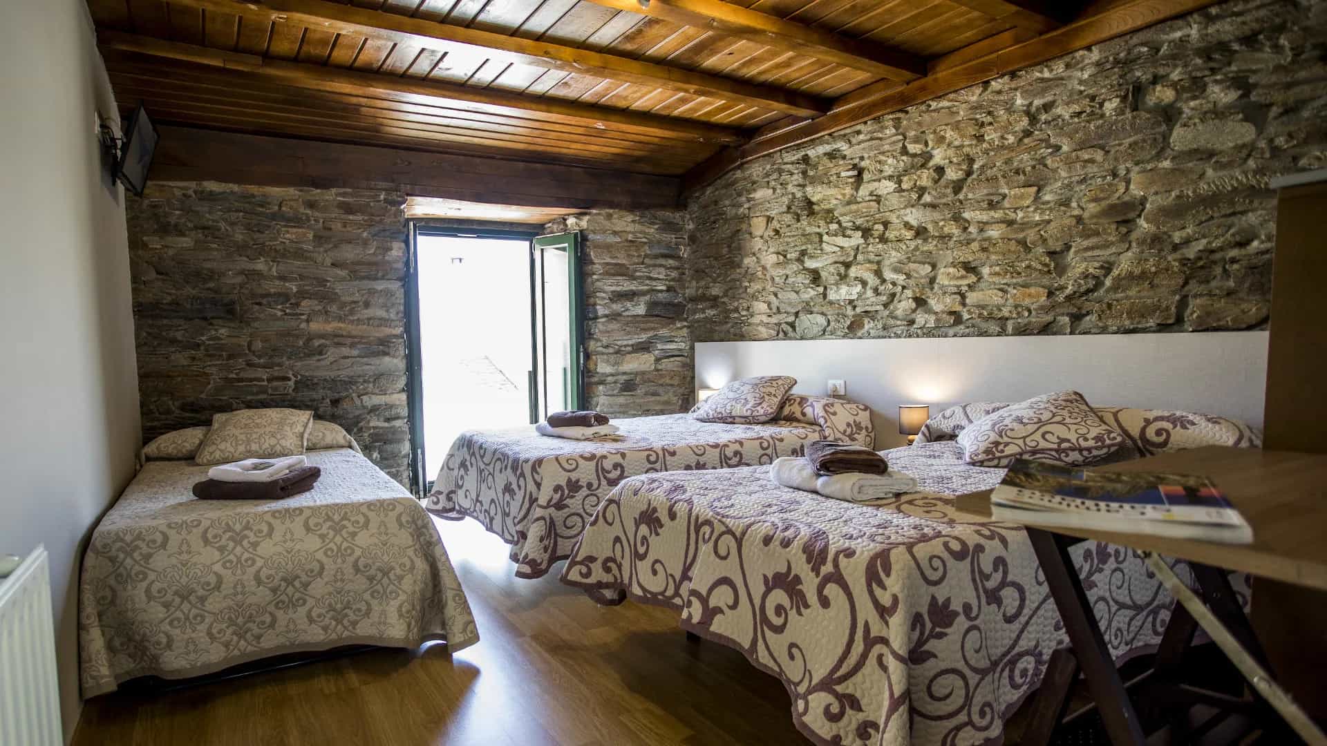 Triple bedroom with stone walls, wood ceiling, and patterned bedspreads, opening to outdoors