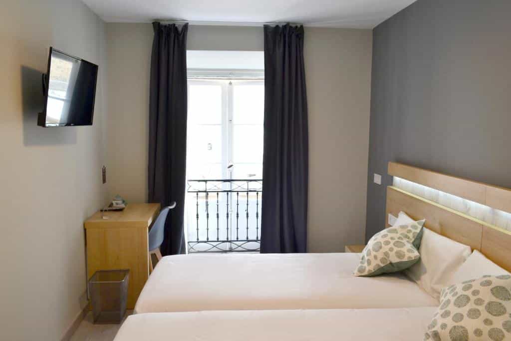 Twin beds and desk in a hotel room with a balcony door in Santiago de Compostela
