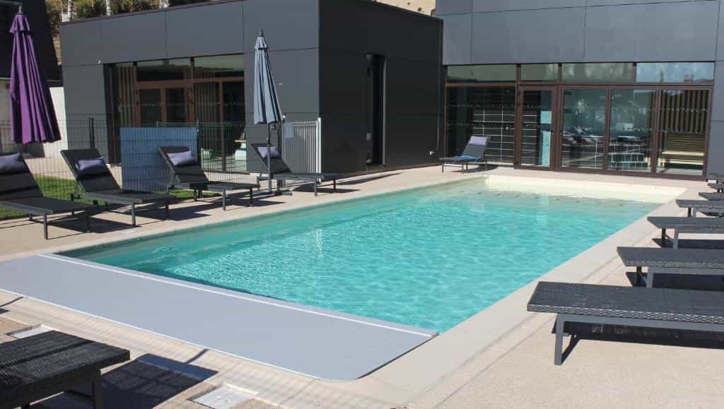 Outdoor swimming pool with lounge chairs and modern dark building facade at Logis Hôtel et Spa Chez Camillou.