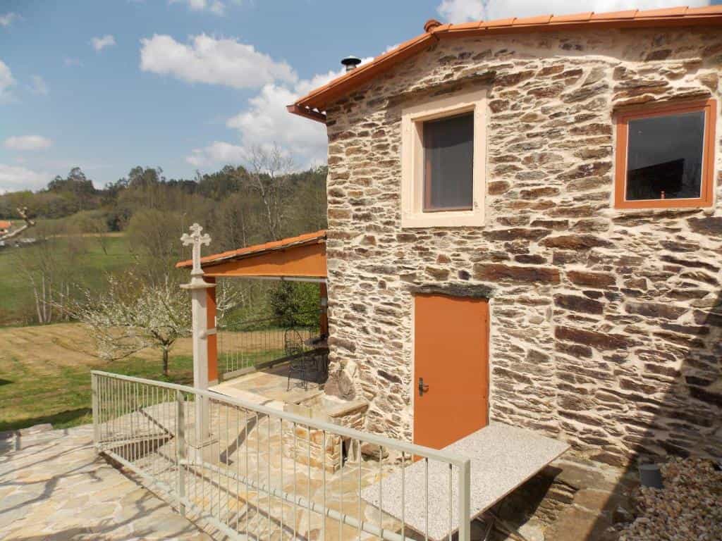 Stone building with orange door and cross monument overlooking green fields near Granja del Peregrino.