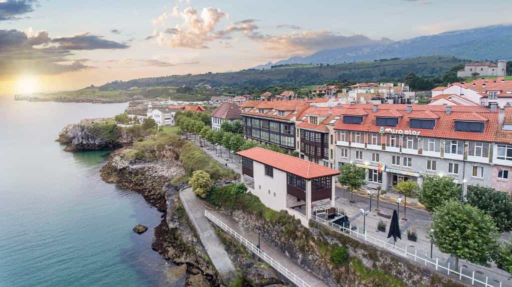Coastal town with red-roofed buildings, promenade, and mountains at sunset