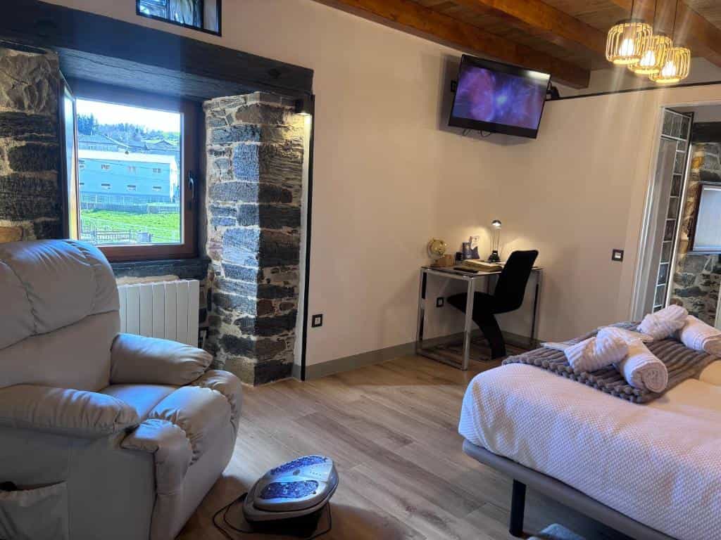 Bedroom with stone accents, light wood floor, recliner, desk, and bed with white towels in Casa Uría, Cam. Santiago.