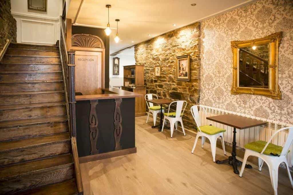 Hotel reception area with wooden stairs, stone wall, and small cafe seating.