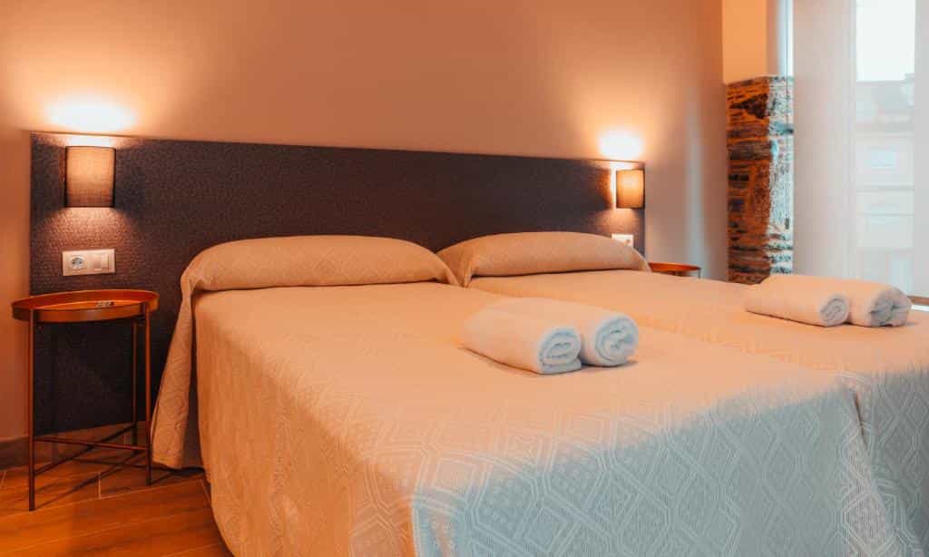 Twin beds with white rolled towels in a warmly lit hotel room with a stone accent wall.