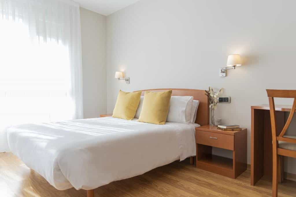 Bedroom in Hostal ALBA Lugo with white linens, yellow pillows, and bright window light.