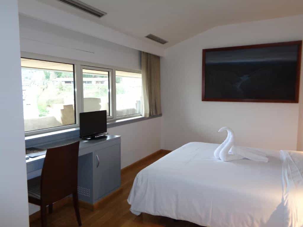 Hotel room with white bedding, towel swan, desk, and framed dark landscape art.
