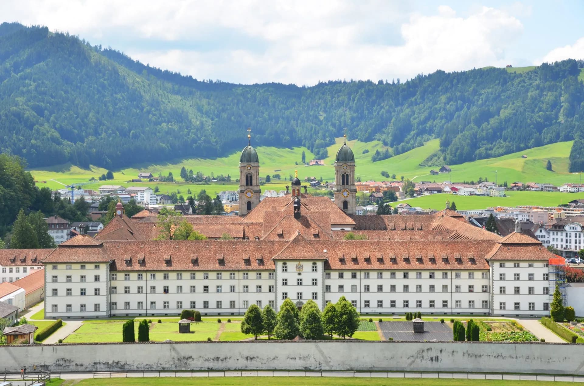 Benedictine Abbey of Einsiedeln with twin towers set against lush green Swiss mountains.
