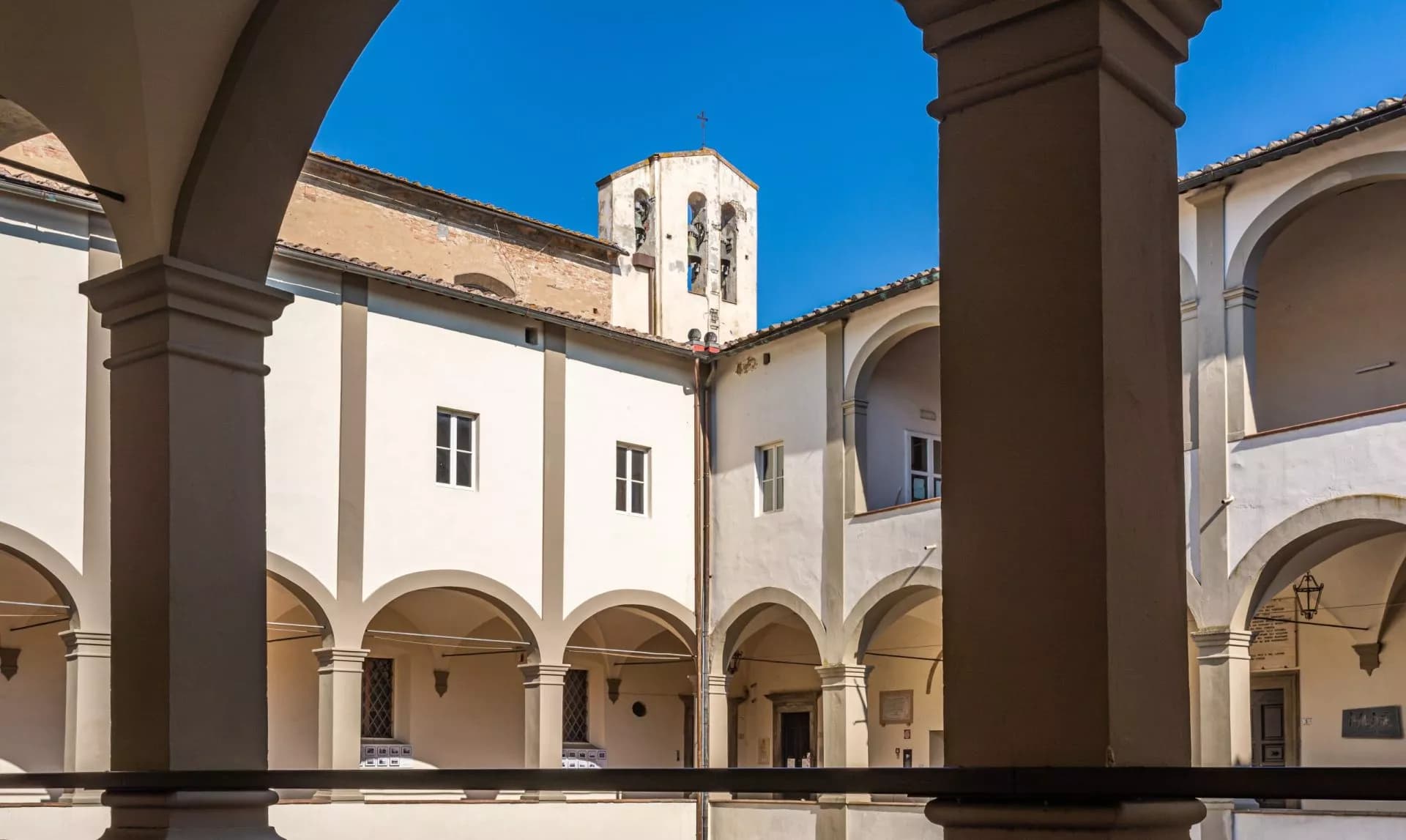 Courtyard of San Domenico Church with arches, white walls, and bell tower under a clear blue sky.