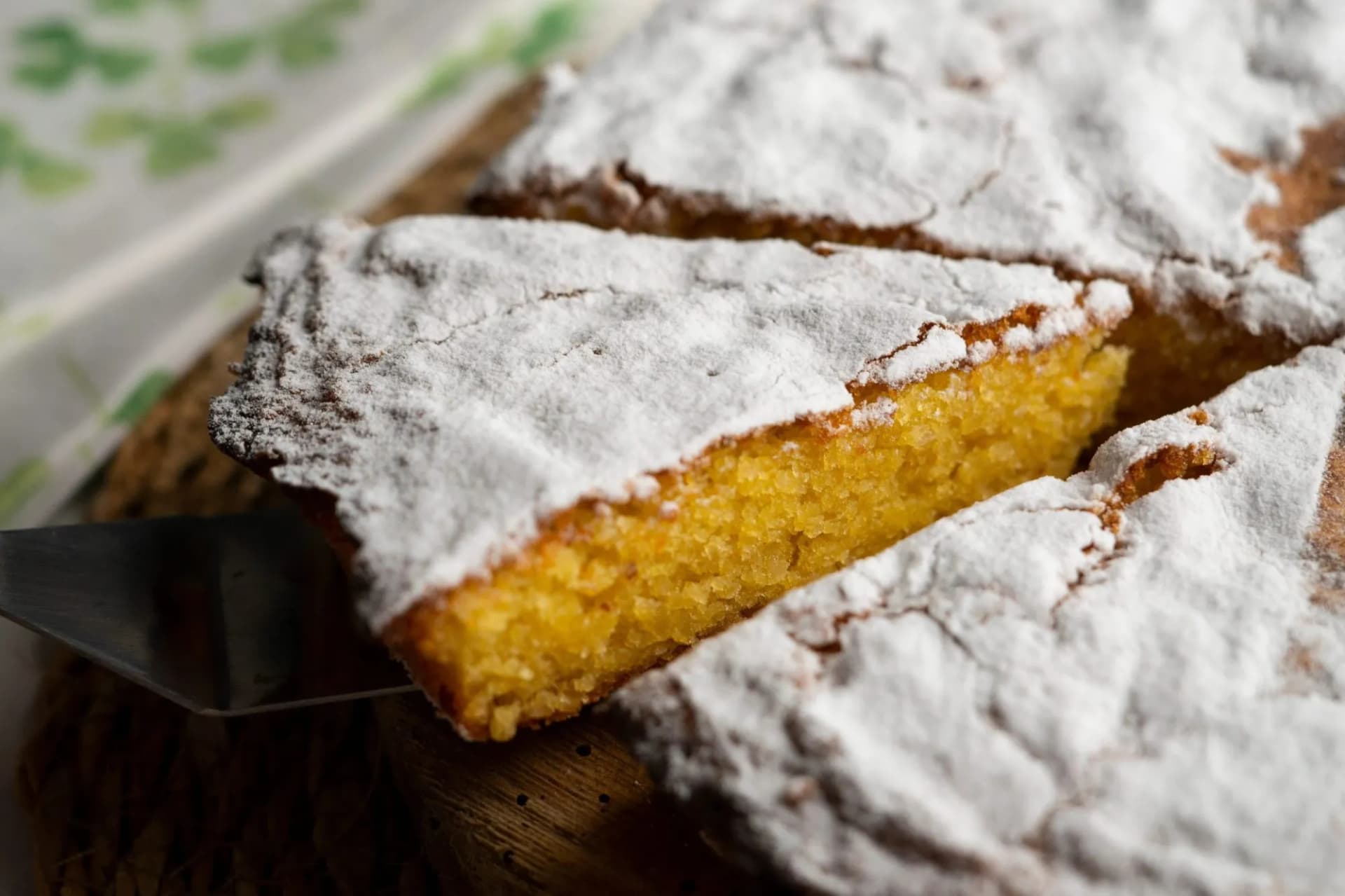 Slice of Tarta de Santiago almond cake dusted with powdered sugar being served.