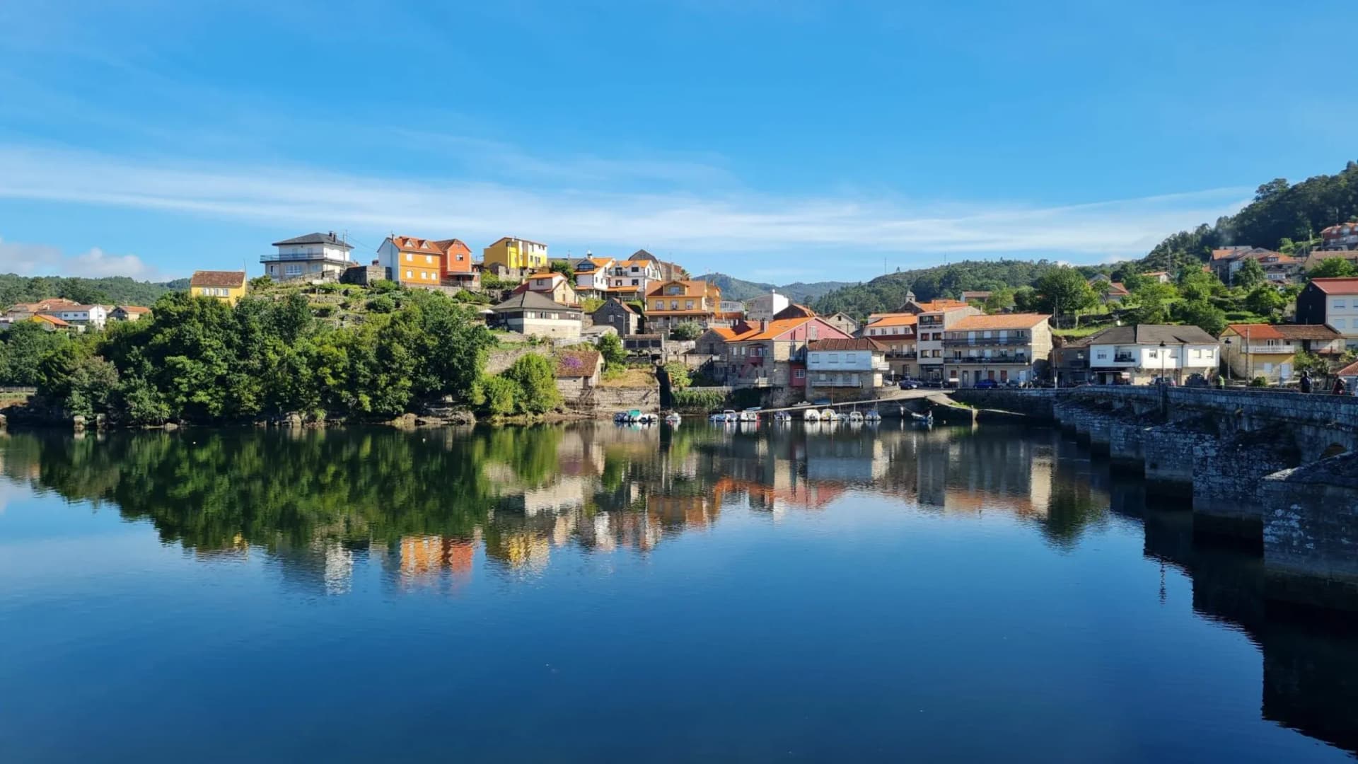 Town with colorful houses on a hill reflected in the calm water of Caldas de Reis.