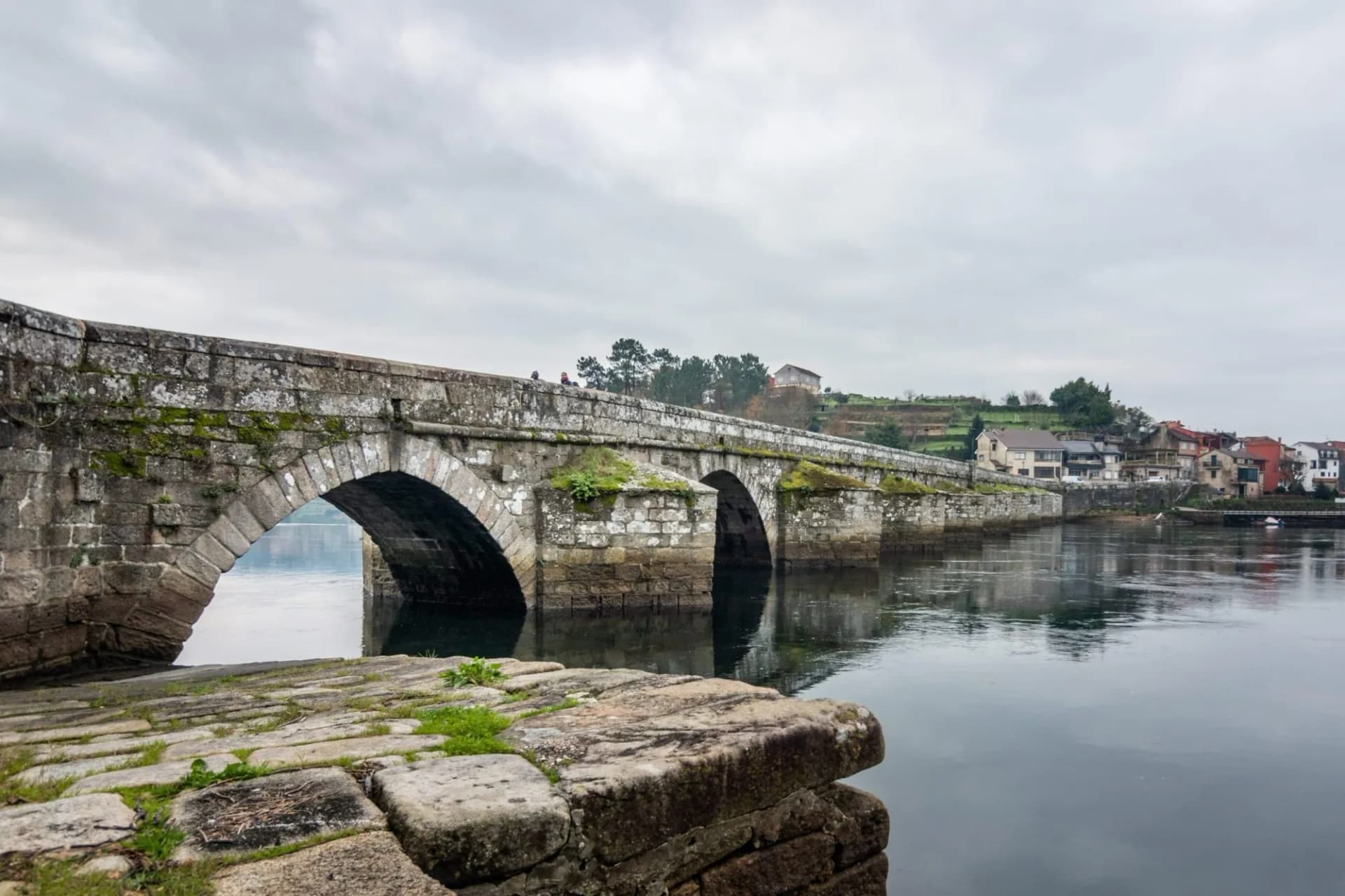 Stone bridge with mossy arches over dark water near Ponte Sampaio village