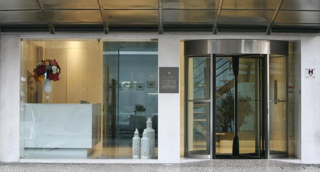Hotel Costa Verde entrance with white reception desk, flowers, and revolving glass door.