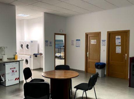 Laundry area with washing machines, round table, and black chairs inside Vilamartín de Valdeorras Municipal Hostel.