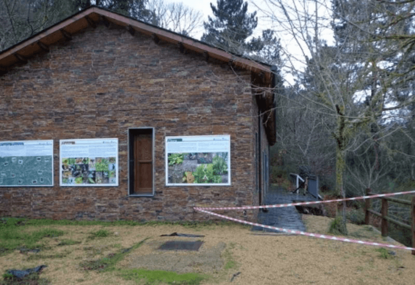 Stone building with information panels next to a wooded area, possibly an albergue in winter.