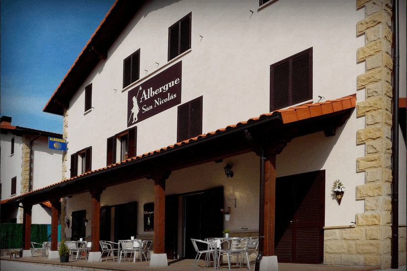 Albergue San Nicolás building with covered porch and outdoor seating under blue sky