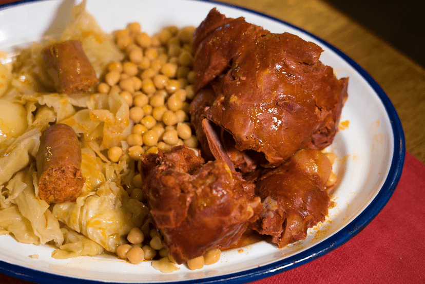 Stew with large pieces of meat, chickpeas, cabbage, and sausage on a white plate.
