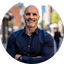 Smiling man in a dark button-down shirt standing on a city street.