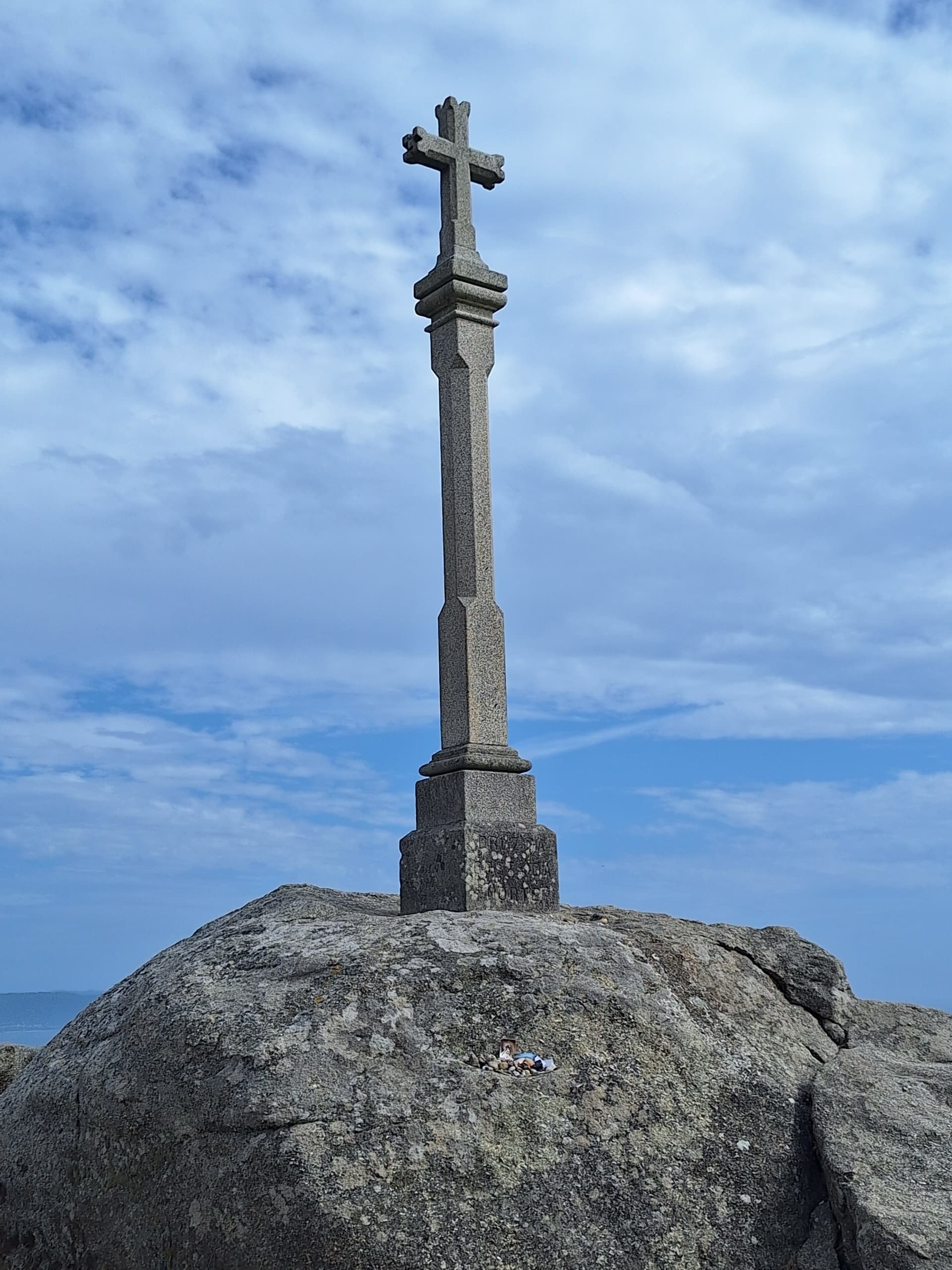 Stone cross monument on rocky cape against a cloudy blue sky
