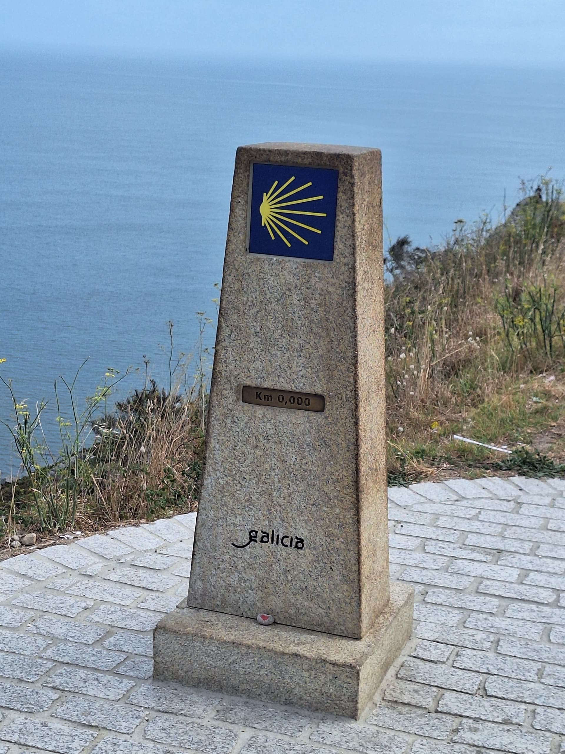Stone zero kilometer marker with yellow scallop shell symbol on Camino de Santiago overlooking the sea