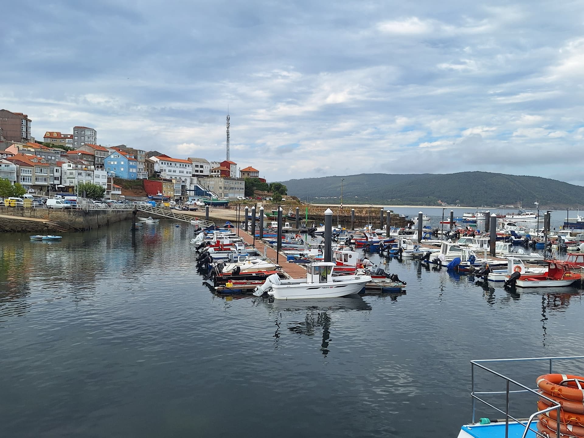 Fishing boats moored in a harbor with a hillside town and mountains in the background.