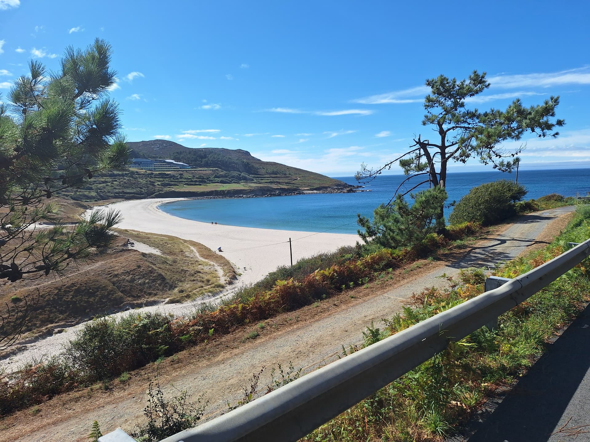 Sandy beach and headland viewed from a coastal road with guardrail