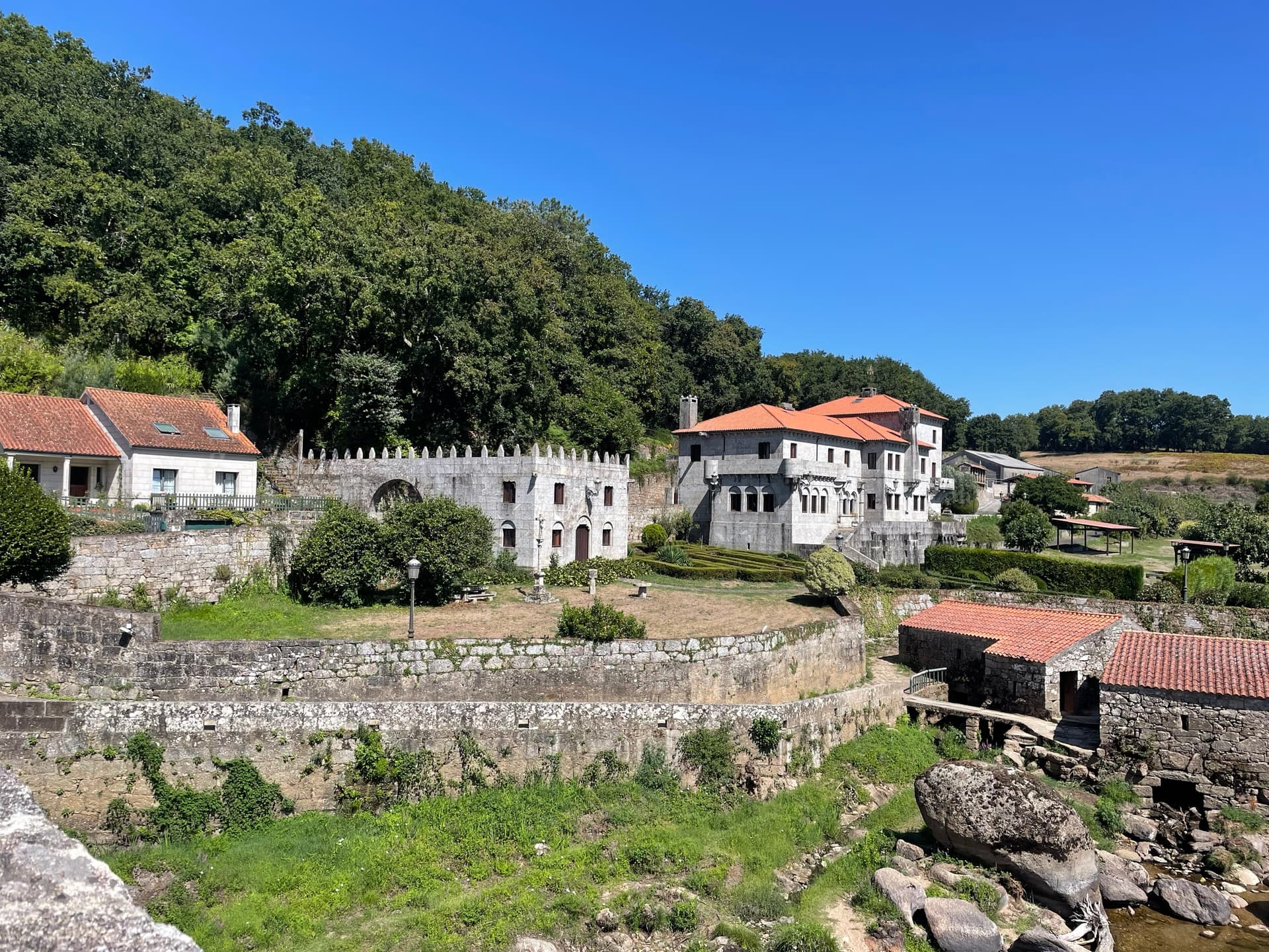 Stone hamlet with orange-tiled roofs beside a rocky river under a clear blue sky