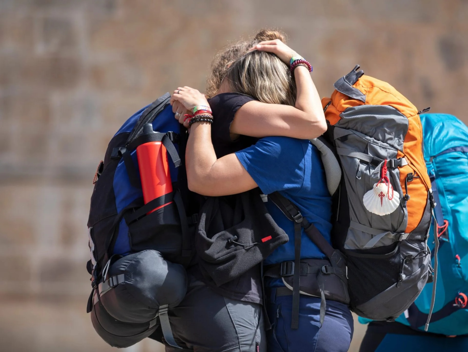 Pilgrims hugging with large backpacks, one featuring a scallop shell, at Plaza del Obradoiro.