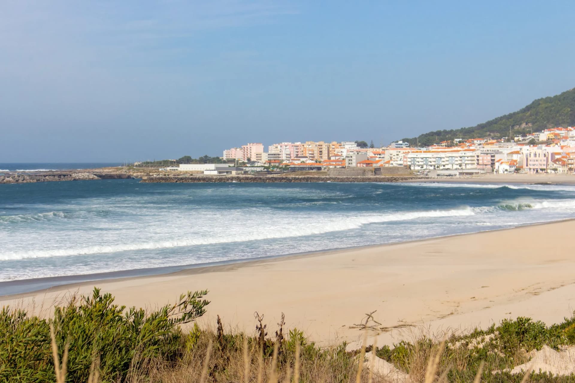 Wide empty beach with beautiful waves and white town on background. Vila Praia de Ancora, Portugal, landmark. Panoramic Atlantic Ocean coast with calm beach. White sand shore. Europe travel concept.