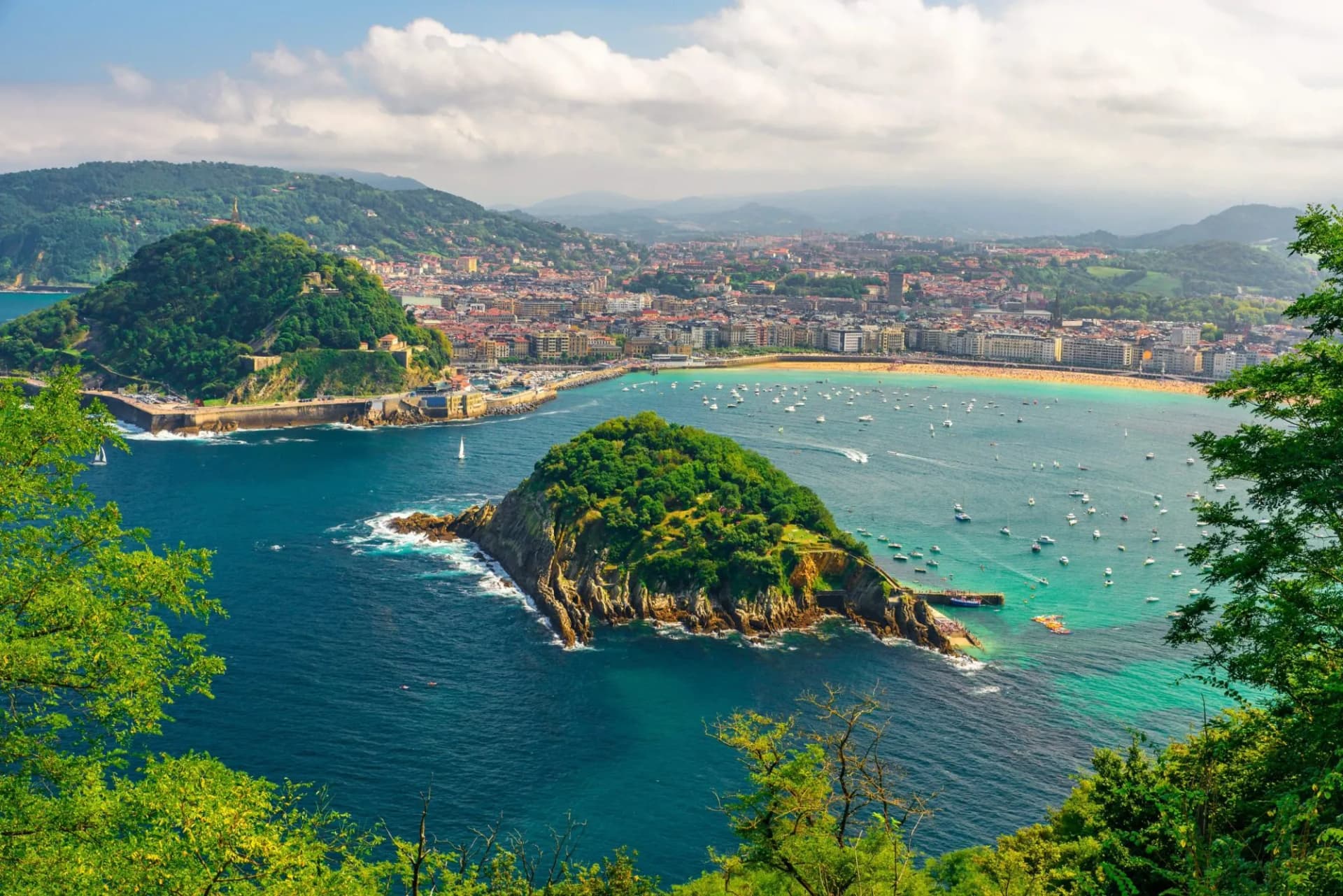 Aerial view of turquoise bay, boats, and green island near San Sebastian city and beach.