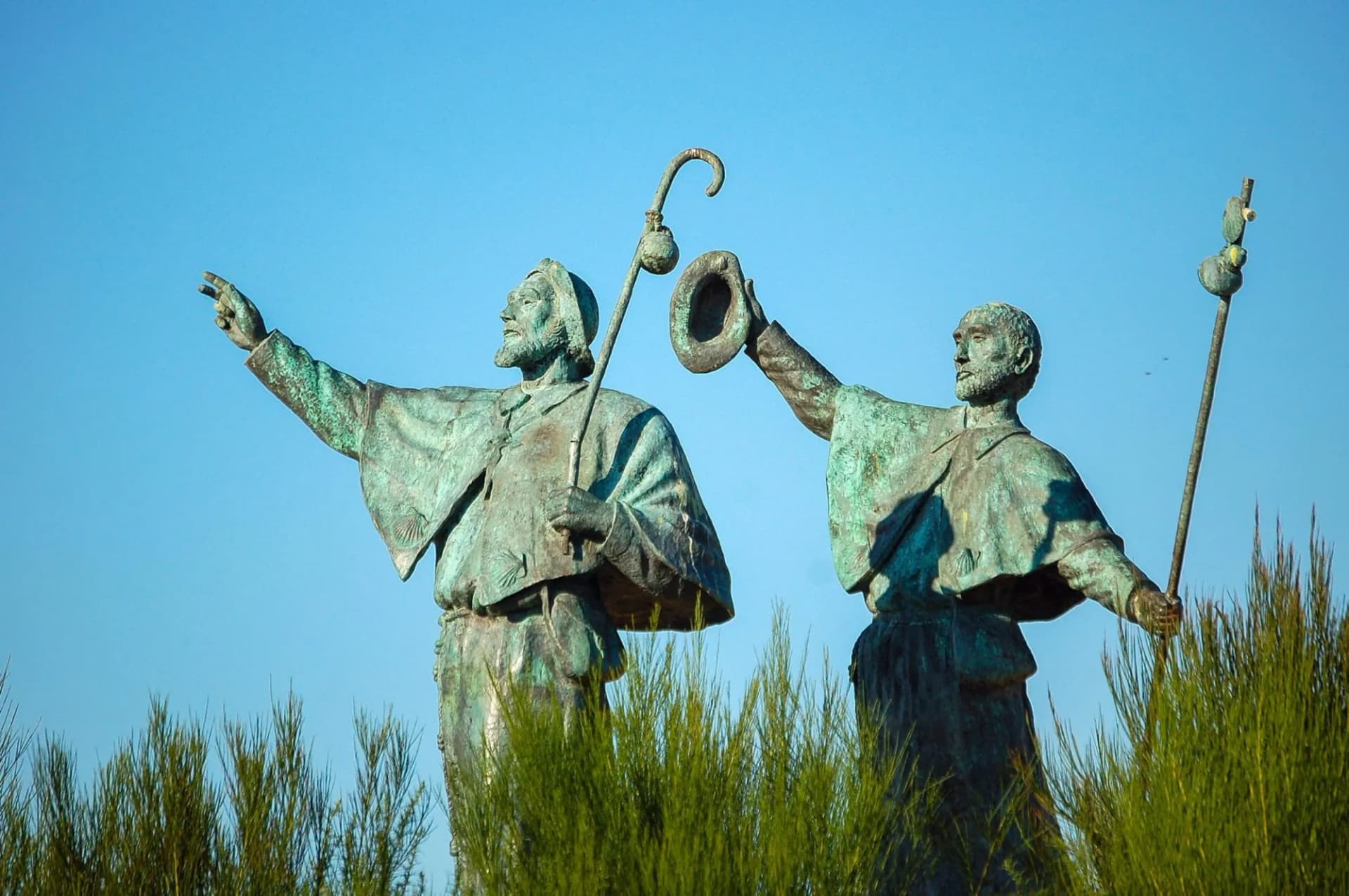 Bronze statue of two pilgrims with staffs against a clear blue sky near Santiago de Compostela.