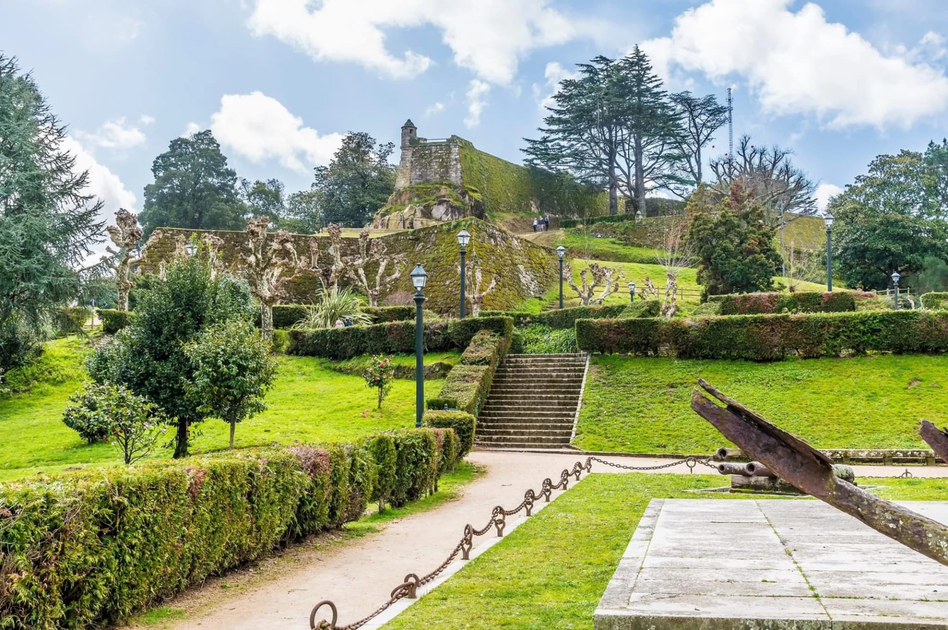 View up towards the moss-covered Castro Castle in Vigo, featuring green lawns, stone steps, and old cannons.