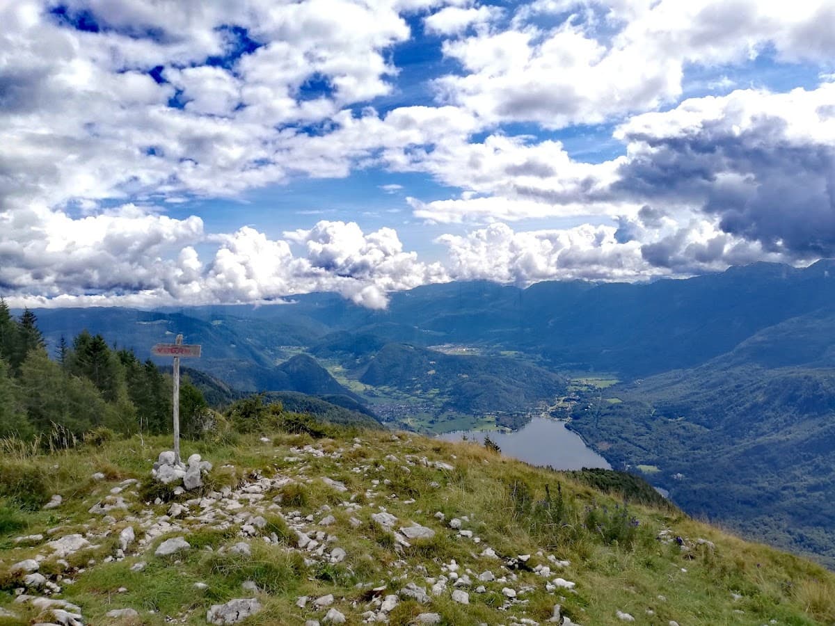 Mountain overlook with trail sign, lake, and valley below under dramatic clouds