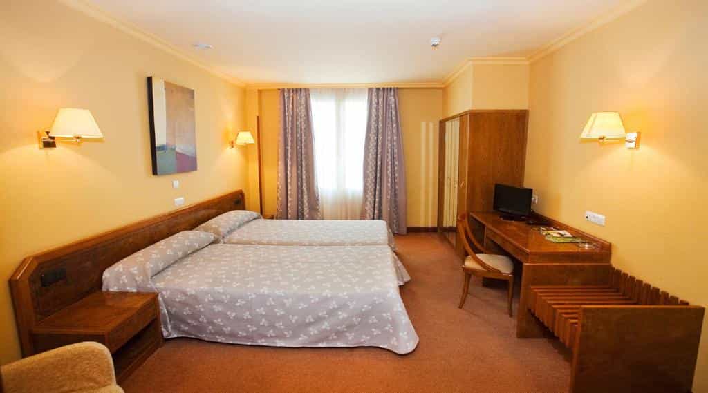 Twin beds in a hotel room with yellow walls, wooden furniture, and a window with curtains.