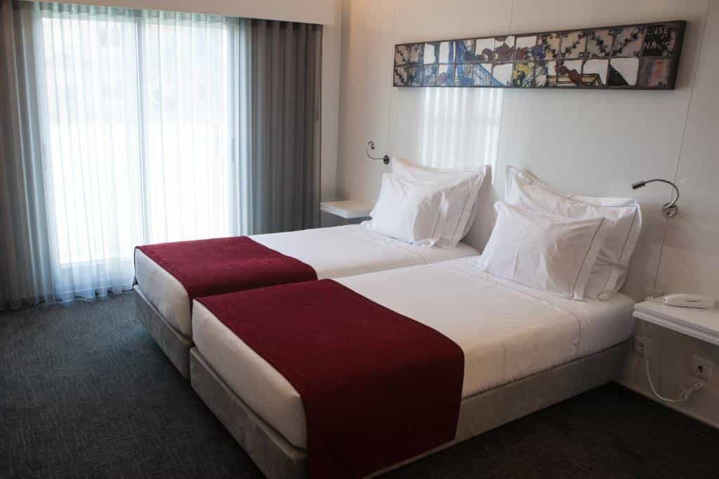 Twin beds with white linens and burgundy runners in a modern hotel room at Hotel Costa Verde.