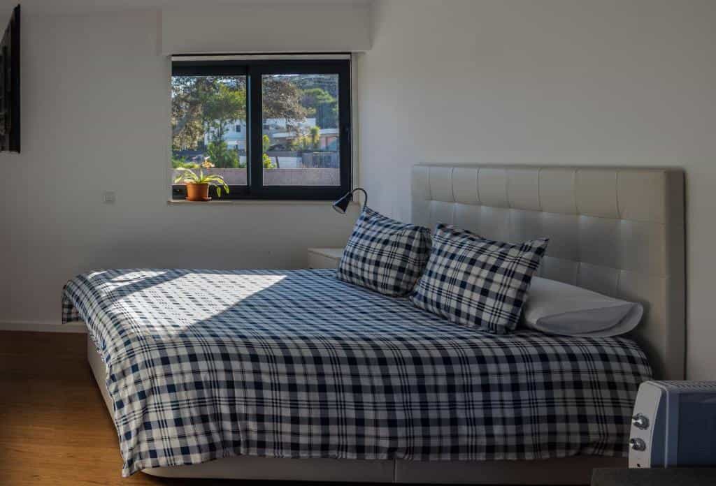 Bedroom with bed, blue plaid bedding, and window showing trees and houses.
