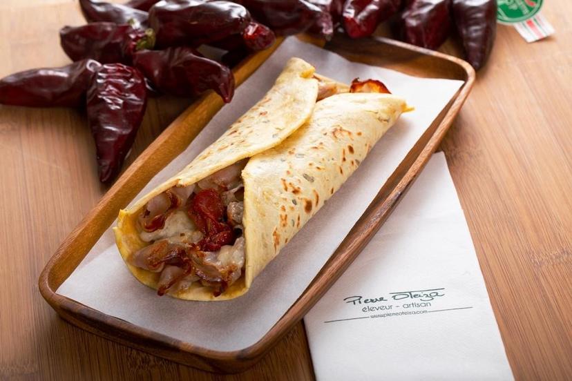 Savory crepe filled with meat and sun-dried tomatoes on a wooden tray with dried chili peppers.