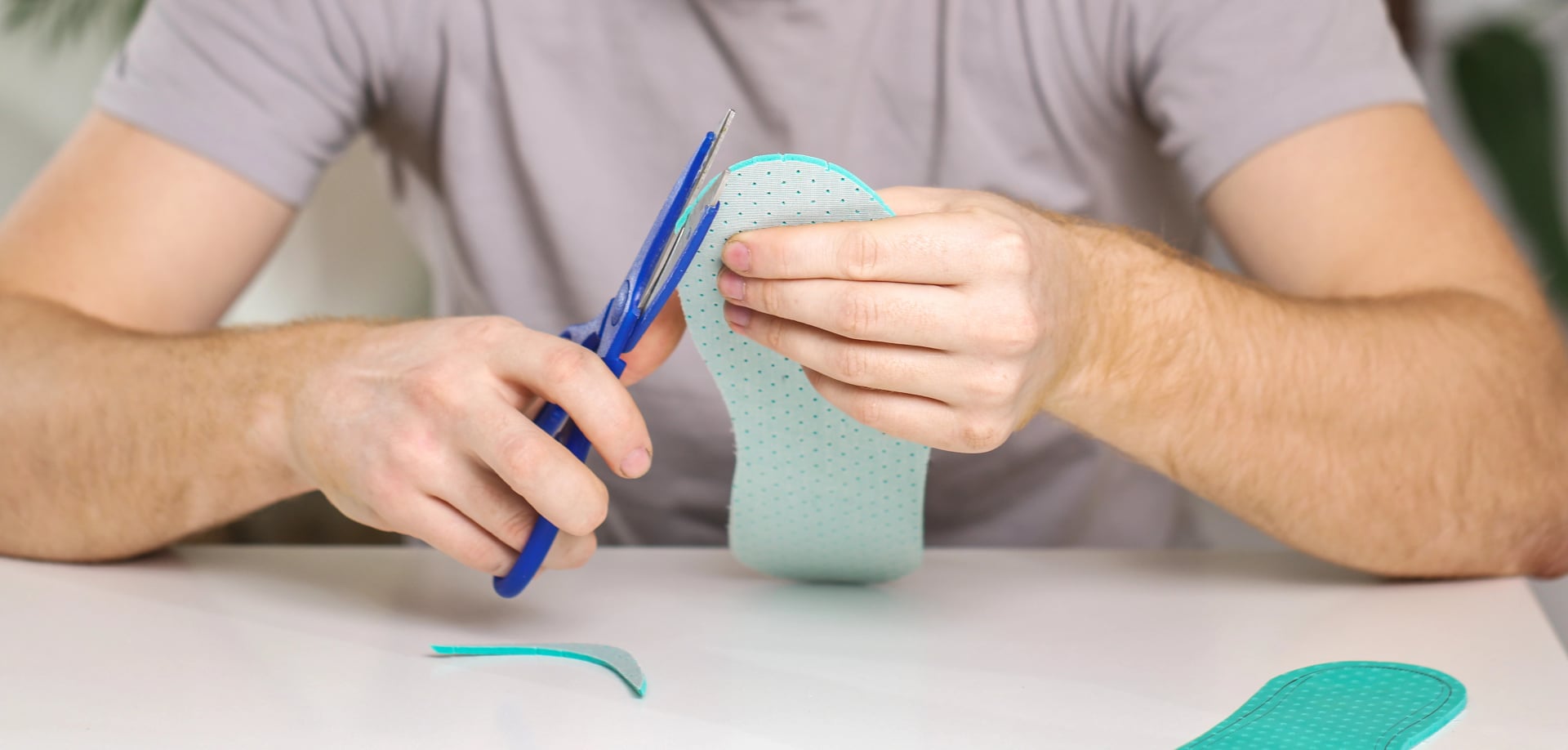 Mann schneidet neue Schuh-Einlegesohlen mit einer Schere aus, um sie an seine Fußgröße anzupassen.