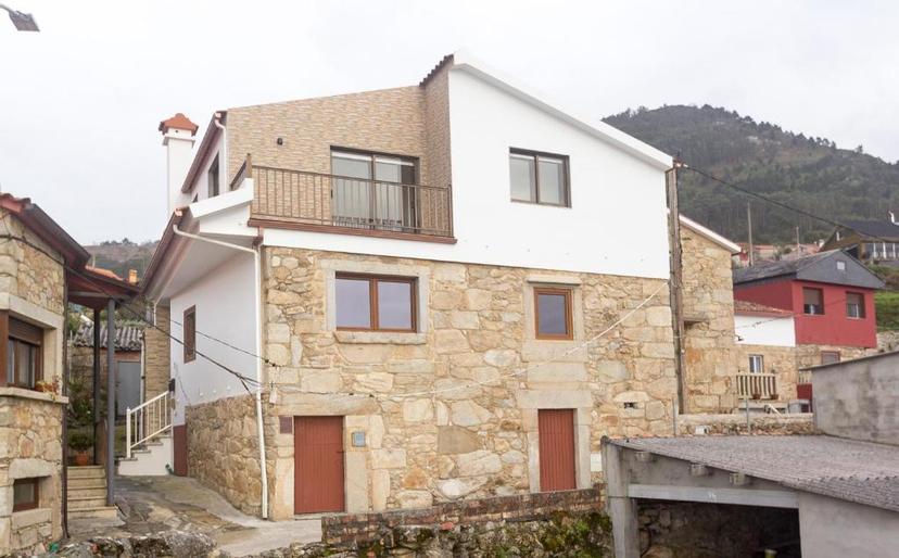 Stone and white renovated house in a village setting with forested mountains in the background.