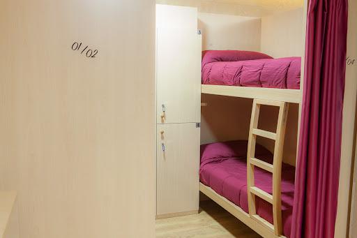 Bunk beds with magenta bedding and privacy curtain inside a hostel room at Albergue Palacio de Merás.