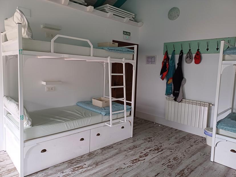 Hostel room with white metal bunk beds, light wood floor, and coats hanging on a rack.