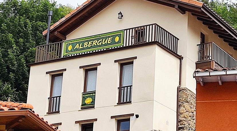Albergue building with "Albergue" banner and scallop shell sign, surrounded by green trees.
