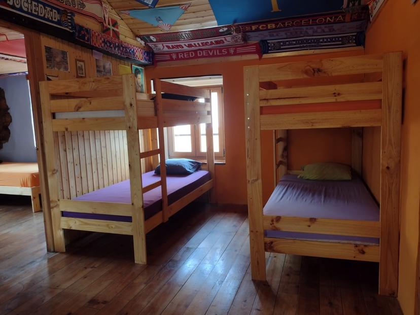 Wooden bunk beds with purple mattresses inside a room decorated with soccer scarves, Albergue de Bodenaya