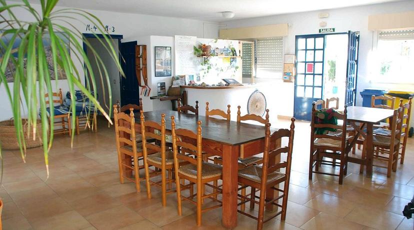 Dining area with long wooden table, rush-seat chairs, and reception counter at Albergue Convento de San José.