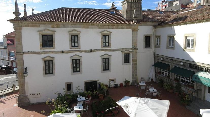 Hotel Monumento Convento de San Benito courtyard with white facade and outdoor seating under sun.
