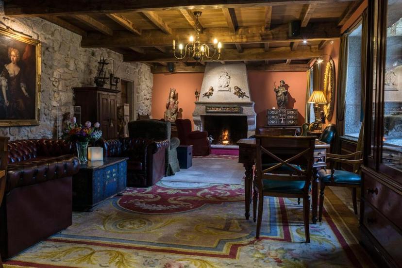 Historic hotel lounge with stone walls, wood beams, fireplace, and antique furniture in Hotel Monumento Convento de San Be...