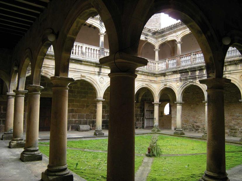 Stone cloister courtyard with arches, columns, and a mossy green center at Monasterio de Zenarruza.