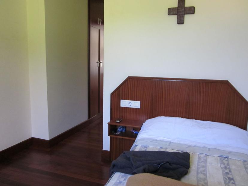 Bedroom with wooden headboard, white walls, and a dark wooden floor, Monasterio de Zenarruza.