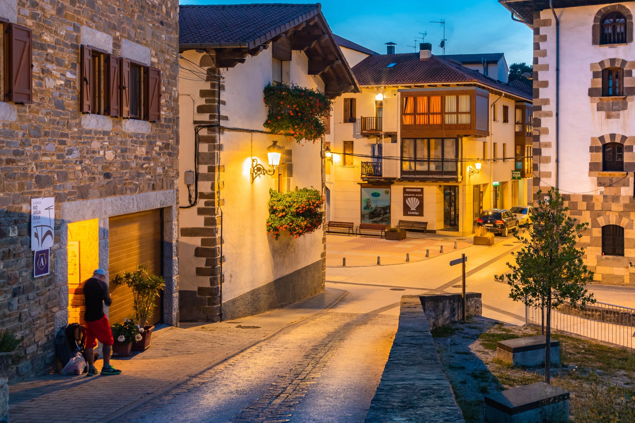 Hiker outside Rio Arga Pilgrim Hostel at Twilight Hour near the Medieval Bridge Entrance into Zubiri, Navarra along the Way of St James Pilgrimage Trail Camino de Santiago