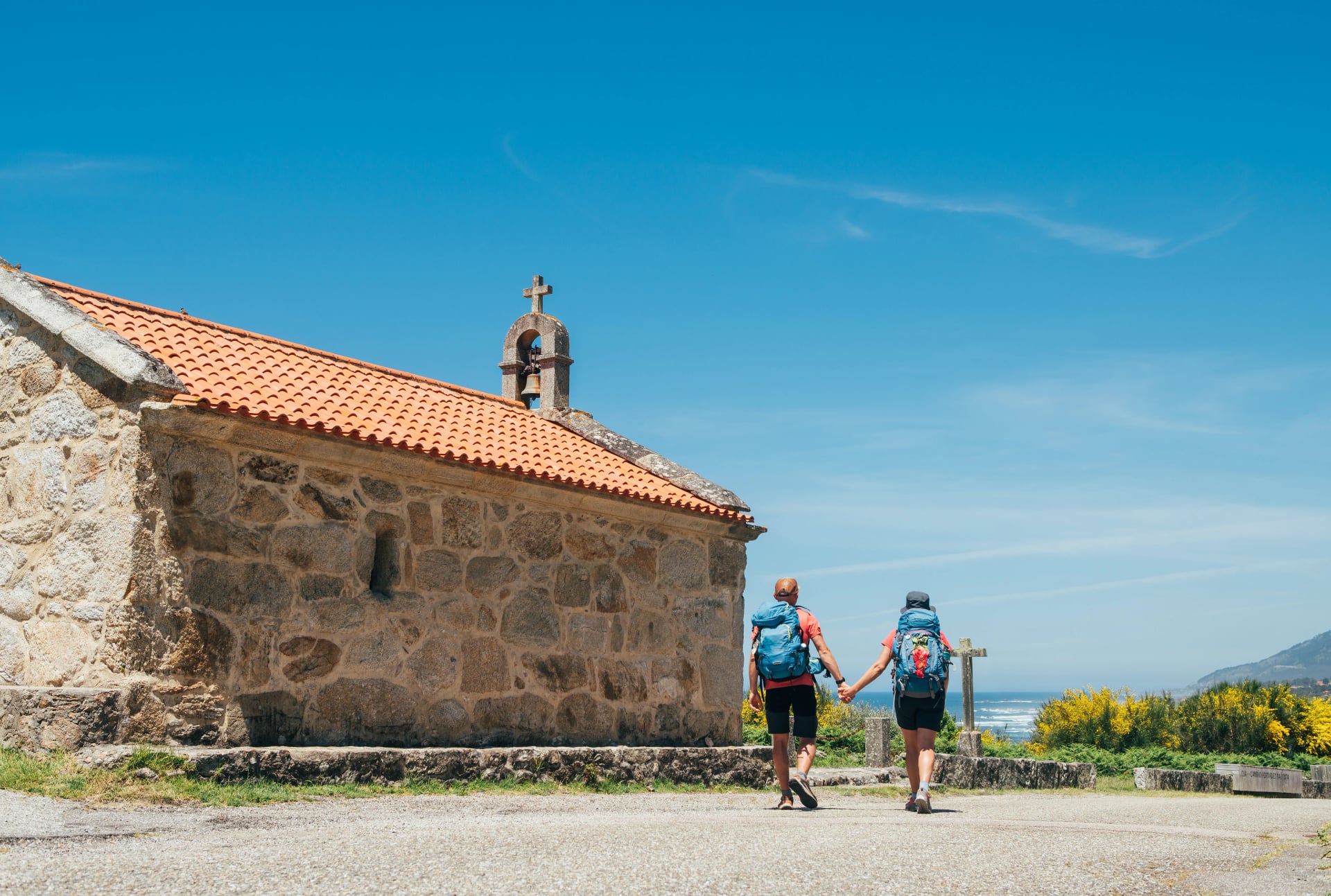 Couple de pèlerins avec des sacs à dos marchant main dans la main à côté d'une vieille église sur le Chemin Portugais, une marche inspirante sur le célèbre Camino de Santiago. Voyage, pèlerinage, style de vie, architecture