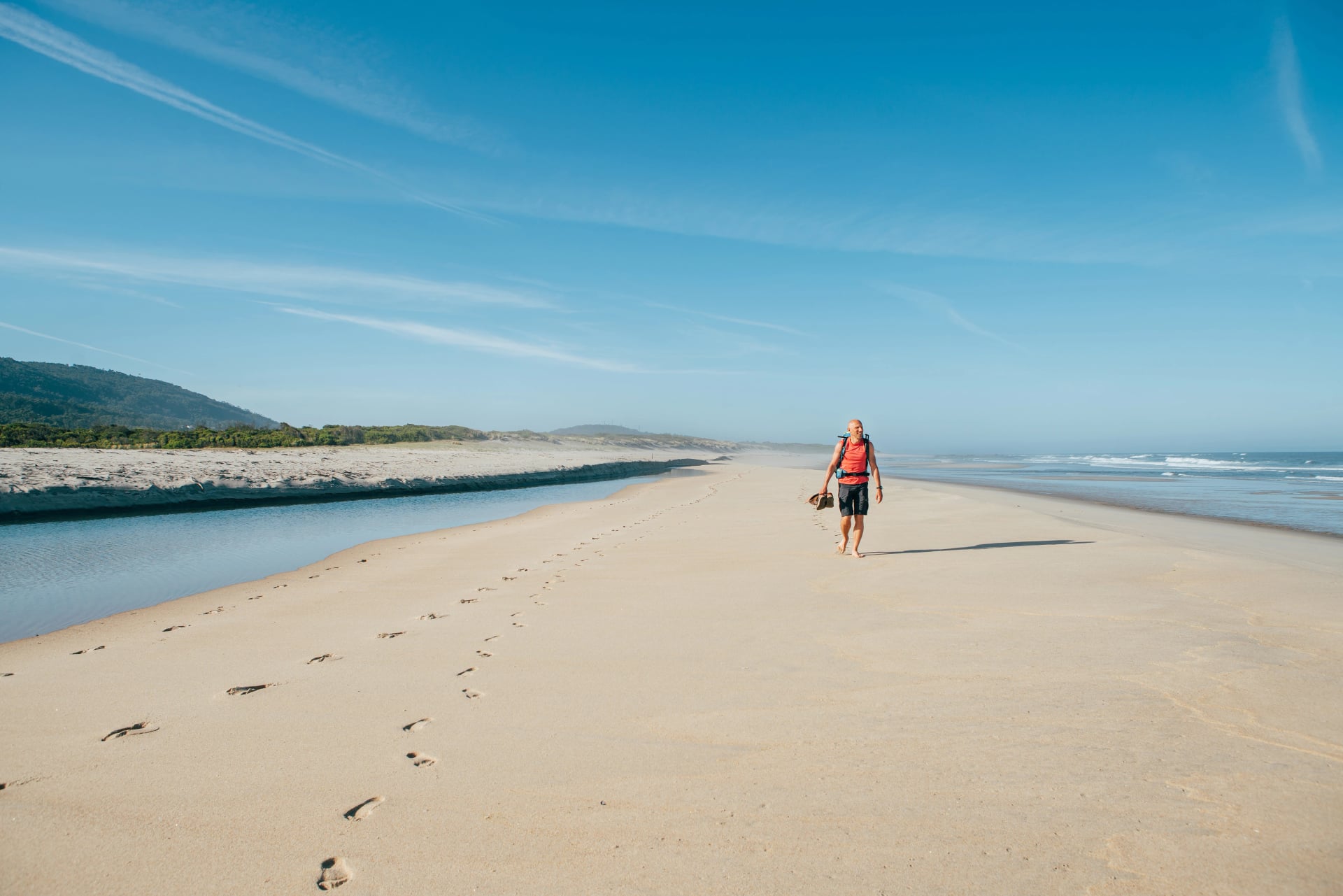 Einsamer barfuß Reisender, der morgens an einem sandigen portugiesischen Strand an der Atlantikküste geht. Aufnahme während des Camino Portugués - beliebte Pilgerroute. Aktive Menschen, Reisekonzept.